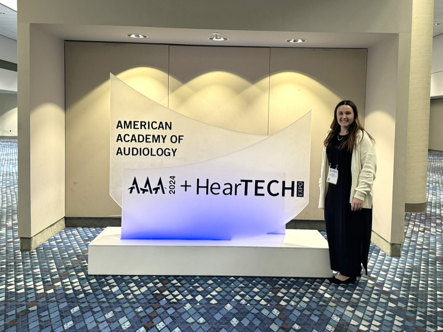 Dr. Belanger stands in front of AAA + HearTech sign at AAA 2024