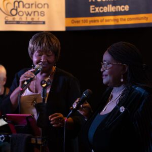 Two women are singing into microphones at a function.