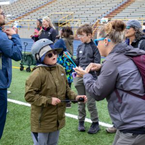 People communicating at outdoor event, wearing jackets.