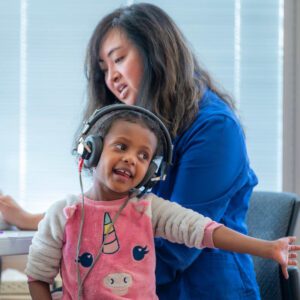 Child with headphones and woman in background.