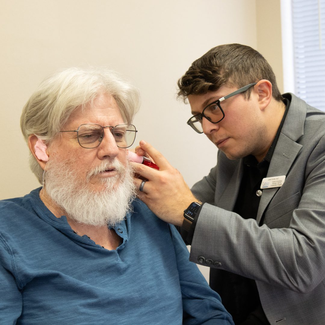 Man adjusting another man's hearing aid.
