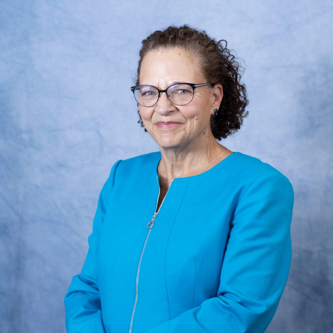 Smiling woman in blue outfit, glasses.