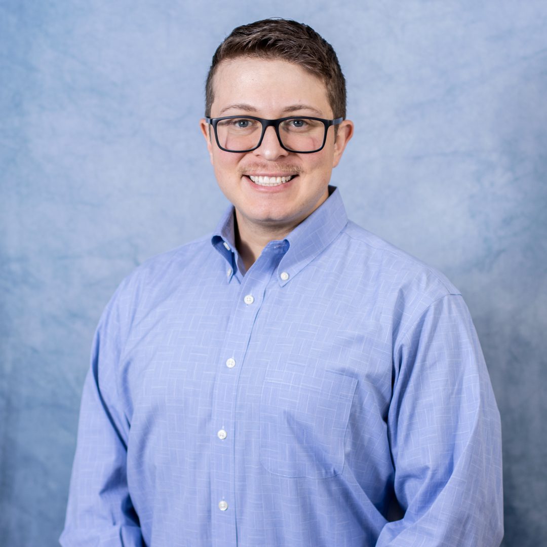 Smiling person in blue button-up shirt.