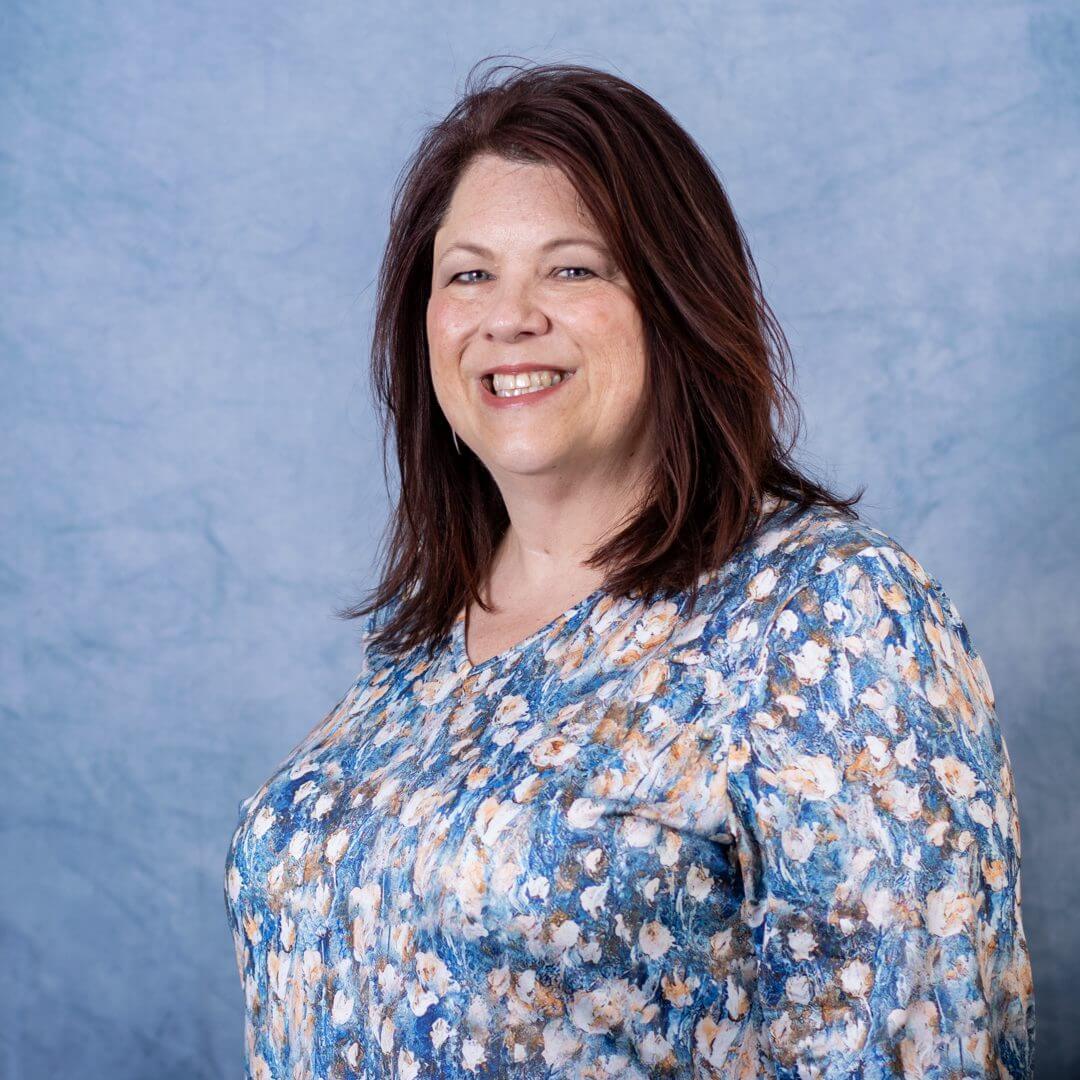 Smiling woman in floral blouse, blue background.